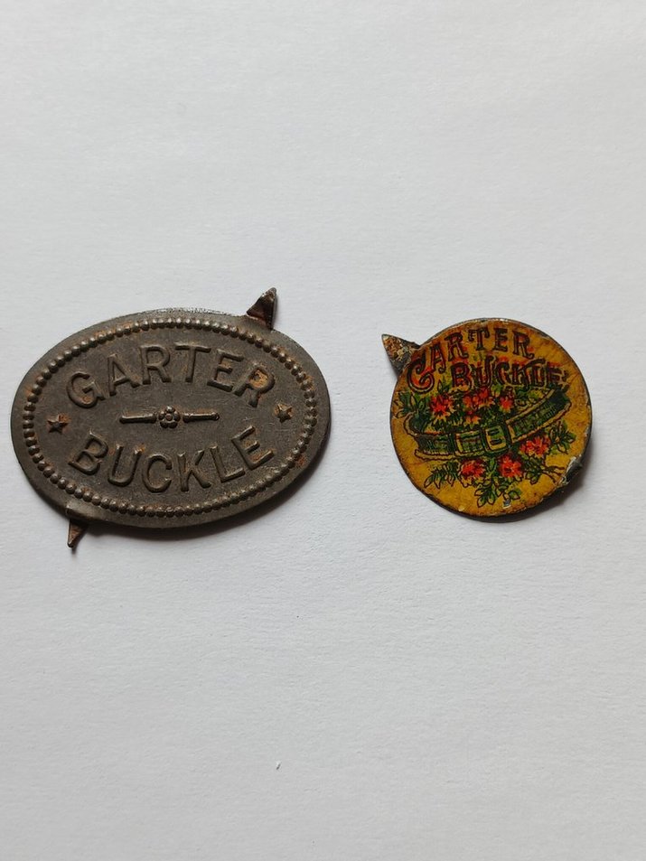 Two Garter Buckle Tobacco Tin Tags, one embossed (left) and one lithographed (right).